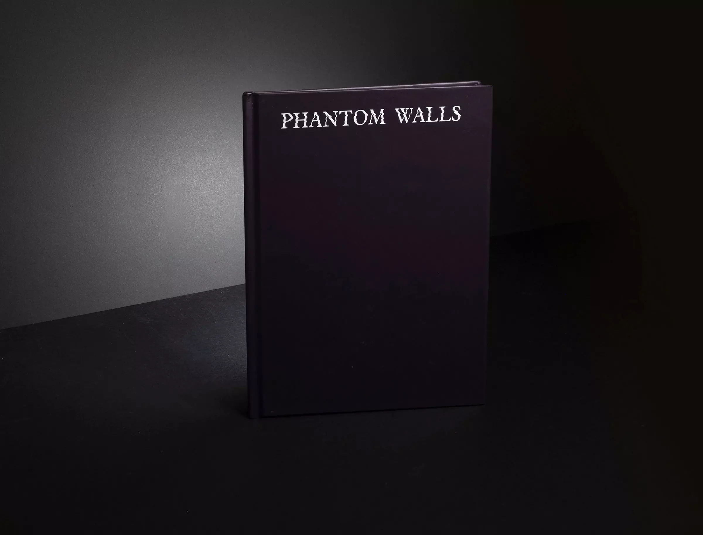 A black book with the title 'Phantom Walls', with light hitting the dark background behind it.