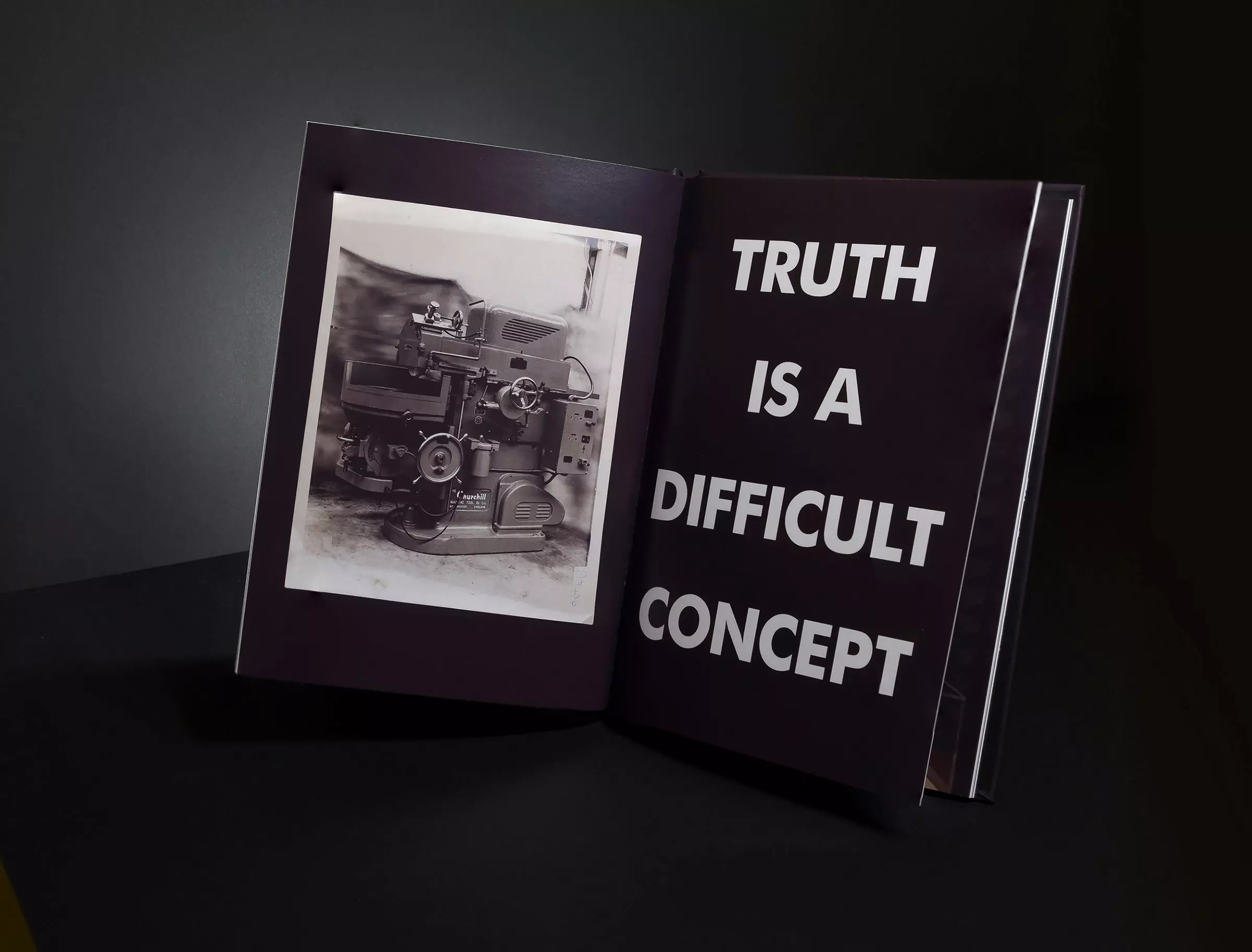 An open book with a photograph of a machine on the left page, and 'TRUTH IS A DIFFICULT CONCEPT' on the right.