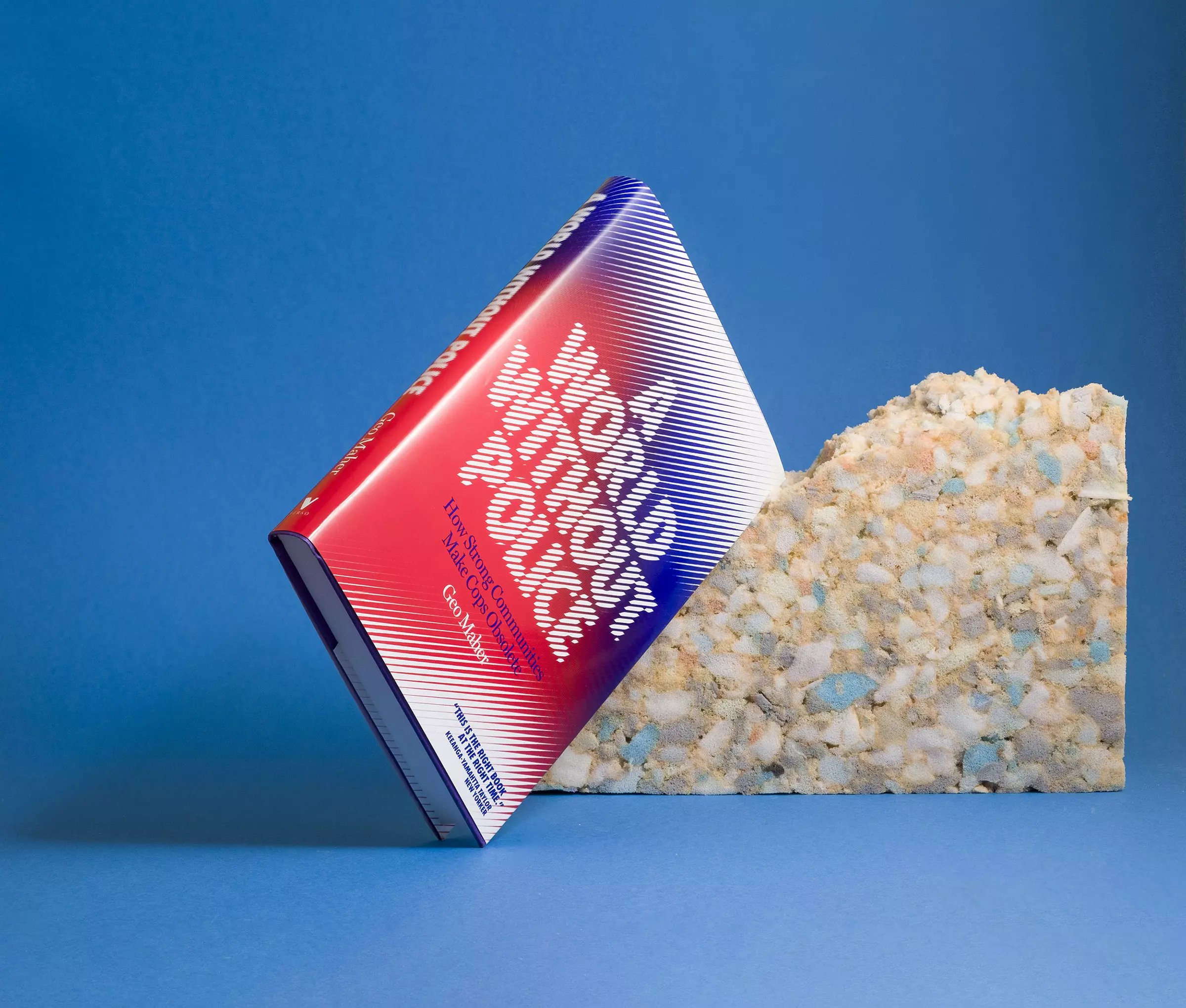 A red, white and blue gradient book colour with text reading 'A World Without Police', leaning against a roughly torn block of packing foam against a light blue background.
