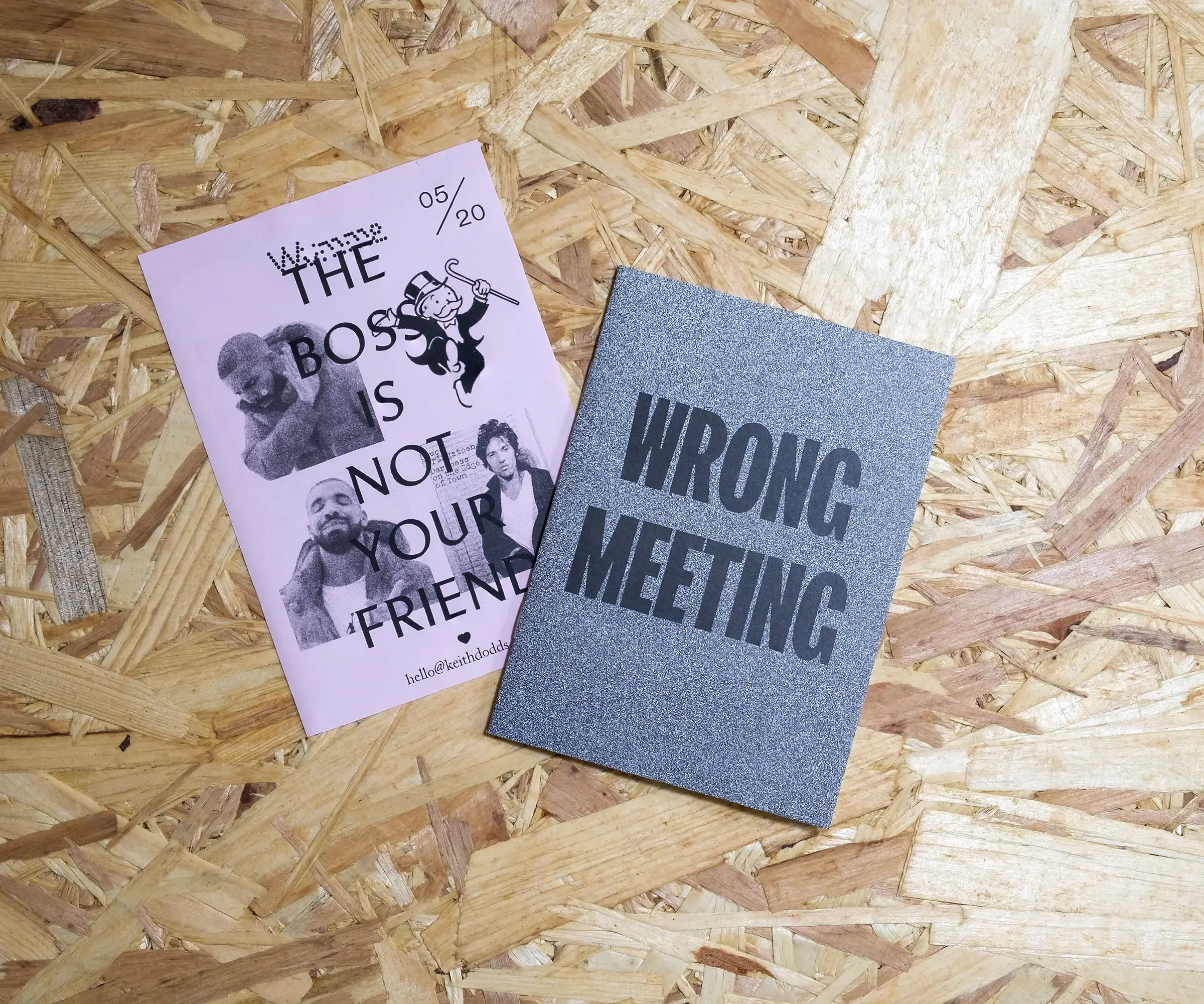 An A6, pink piece of paper featuring the Drake meme, in which Drake shuns Rich Uncle Pennybags from Monopoly, but points approvingly at Bruce Springsteen. The overlaid text reads 'The boss is not your friend'. Beside it is an A6, black and white booklet with the words 'WRONG MEETING' on the cover. Both sit on a background of OSB.