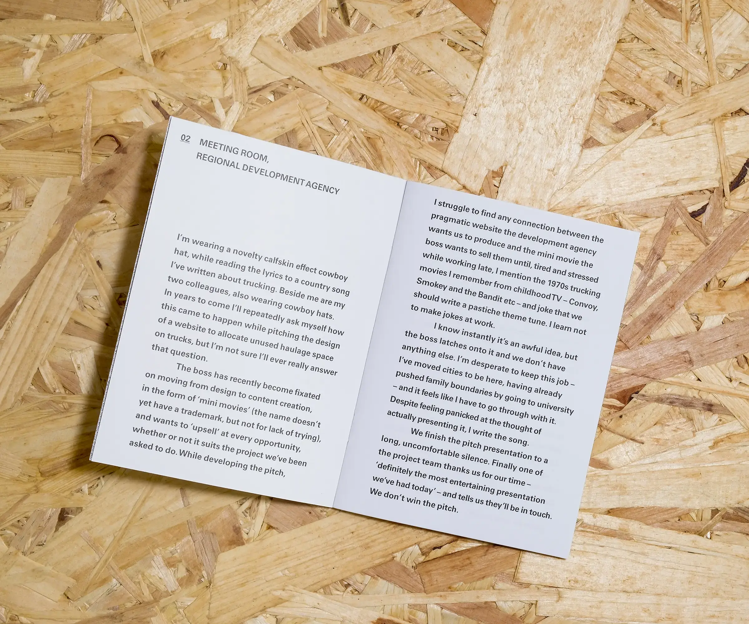 An open A6 booklet, with white pages and small, simply typeset black text on a background of OSB.