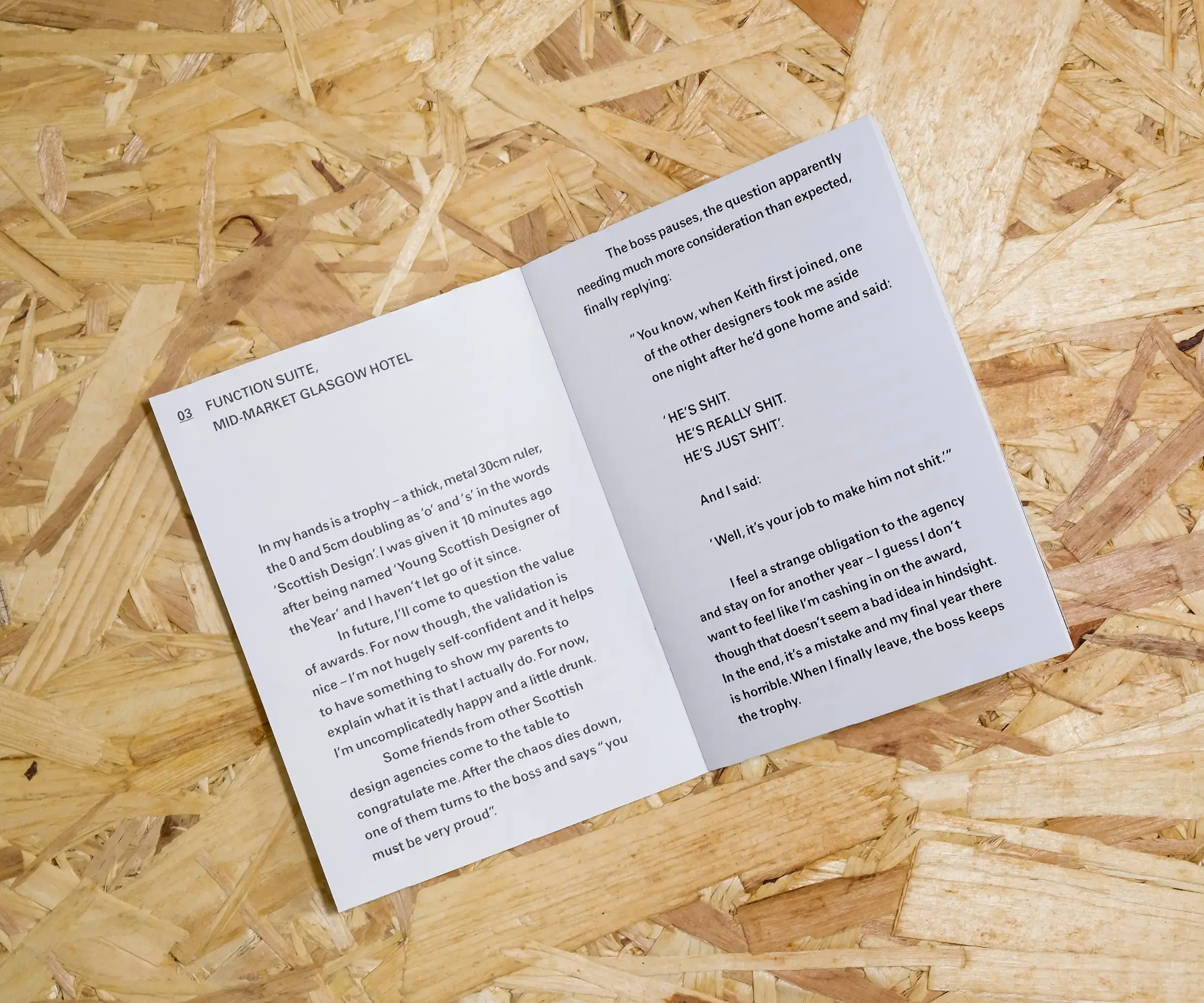 An open A6 booklet, with white pages and small, simply typeset black text on a background of OSB.