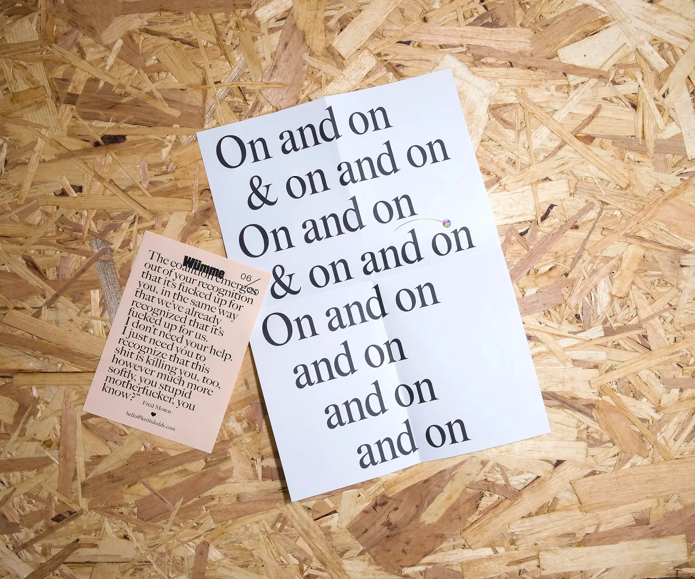 An A4, folded piece of white paper with text reading 'On and on & on and on & on and on. On and on and on and on and on', and a 'spinning wheel of death' icon from the Apple operating system, which appears to bounce across the words like a karaoke machine. Beside it is a smaller, A6 piece of peach paper with a dense quotation from Fred Moten on it. Both sit on a background of OSB.