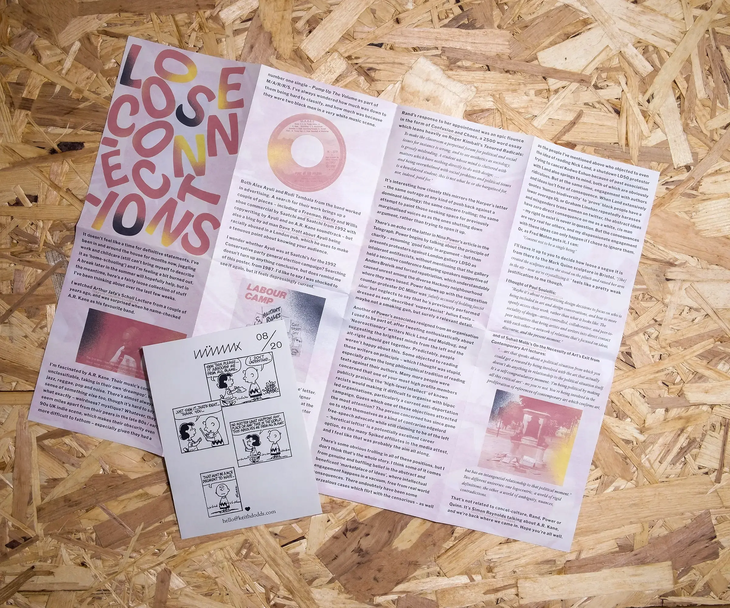 A white, A6 piece of paper features an excerpt from a Peanuts comic strip. Behind it, a much larger sheet of folded white paper has a densely typset text interspersed with images, and the randomly arranged title 'LOOSE CONNECTIONS'. Both sit on a background of OSB.