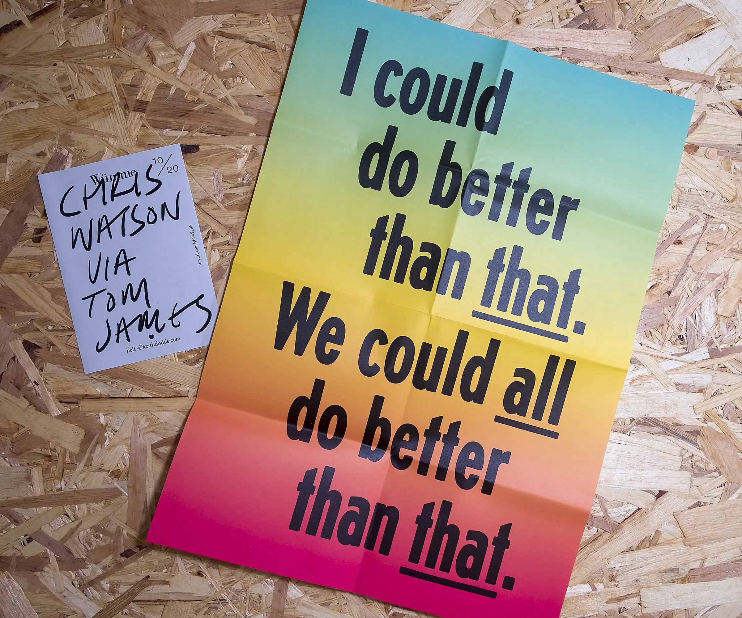 A white, A6 piece of paper with the hand-written text 'Chris Watson via Tom James'. Beside it is an A2, folded piece of paper with a blue, yellow and red gradient background, and the text 'I could do better than that. We could all do better than that'. Both sit on a background of OSB.